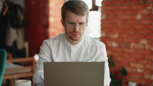 serious man in cafe is chatting online by laptop, typing message in chat online and sending email