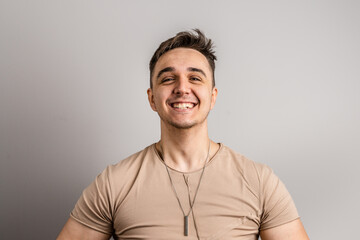 Fototapeta premium Portrait of one adult caucasian man 25 years old looking to the camera in front of white wall background smiling wearing casual t-shirt copy space