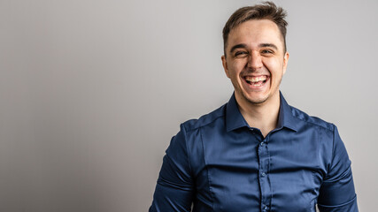 Portrait of one adult caucasian man 25 years old looking to the camera in front of white wall background smiling wearing casual blue shirt copy space