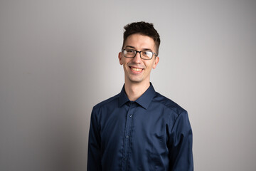 Obraz premium Portrait of one adult caucasian man 25 years old with eyeglasses looking to the camera in front of white wall background smiling wearing casual shirt copy space