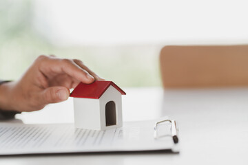 Close up wooden toy house with man signs a purchase contract or mortgage for a home, Real estate...
