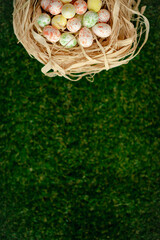 Easter background with colorful yellow, pink, blue Easter eggs in woven basket and green grass. Top view with copy space. Easter holidays banner and header.