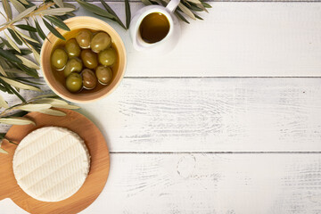 Fototapeta na wymiar Set of green olives with olive oil and white cheese on white wooden background. Healthy Mediterranean food. Top view, flat lay, copy space
