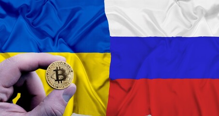 Hand holding a phisical gold bitcoin coin symbol of cryptocurrency on the flag of Russia and Ukraine