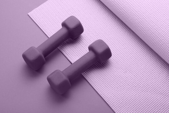Pair of dumbbells and yoga mat on color background
