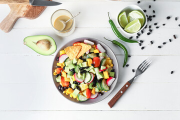 Plate of delicious Mexican vegetable salad and ingredients on white wooden background