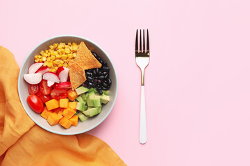 Bowl of tasty Mexican vegetable salad with black beans, radish and nachos on pink background