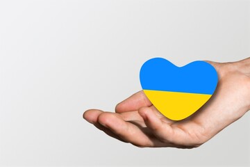 Hands holding ukraine flag in form heart  on background