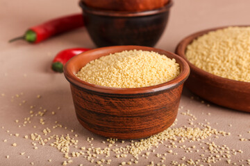 Bowl of raw couscous on color background