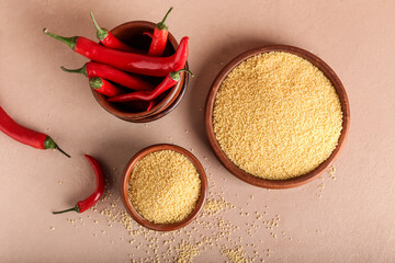 Raw couscous with chili on color background