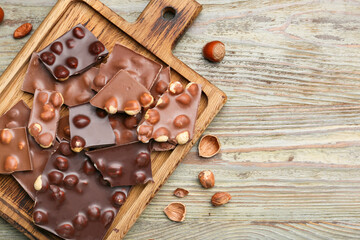 Board with pieces of tasty chocolate and hazelnuts on table