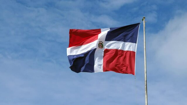 Flying and waving flag of Dominican Republic on wind on blue sky background