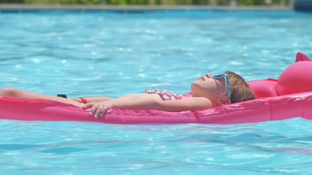 Young child girl relaxing on summer sun swimming on inflatable air mattress in swimming pool during tropical vacations. Summertime activities concept