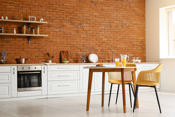 Interior of modern kitchen with dining table, white counters and brick wall
