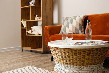 Bottle of water with glasses and magazines on rattan table in living room