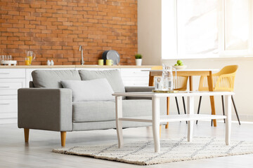 Jug of water with glasses on table and sofa in kitchen