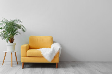 Yellow armchair with fluffy plaid and houseplant near light wall