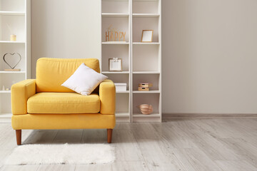 Yellow armchair with pillow and shelving units near light wall