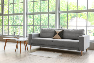 Grey sofa with pillow and tables near big window