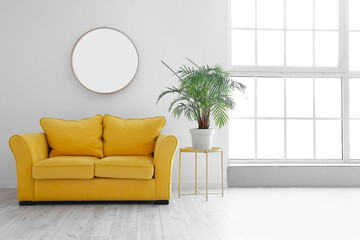 Comfy yellow sofa and table with houseplant near light wall