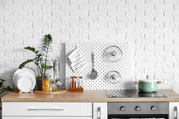 Counter with utensils and houseplant near white brick wall in kitchen