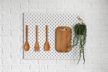Pegboard with wooden utensils and houseplant on white brick wall