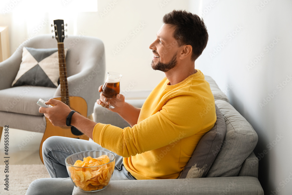 Sticker Handsome man drinking beer while watching TV at home