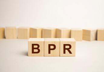 Three wooden cubes with letters - BPR - short for Business process reengineering, on blue table, space for text in right. Front view concepts, flower in the background.