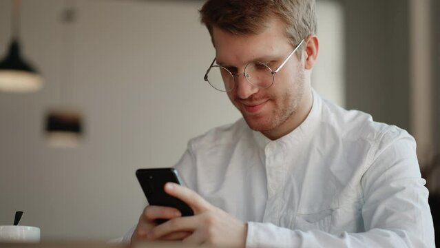 attractive man with glasses is viewing funny pictures and video in social media on smartphone display in cafe