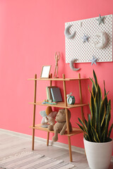 Shelving unit with toys, houseplant and pegboard hanging on pink wall