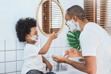 Loving African American Father and little boy having fun playing shaving foam on their faces in bathroom together, Happy African Dad and son.
