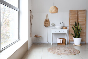 Interior of light bathroom with sink, bag and houseplant