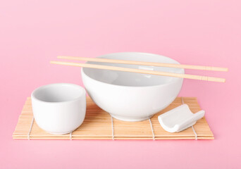 Bamboo mat with Chinese bowls with chopsticks on color background