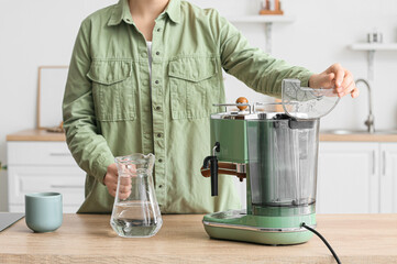 Young woman with jug of water and coffee machine in kitchen