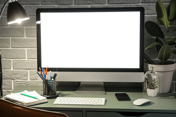 Workplace with modern computer, mobile phone, stationery supplies and glowing lamp near grey brick wall