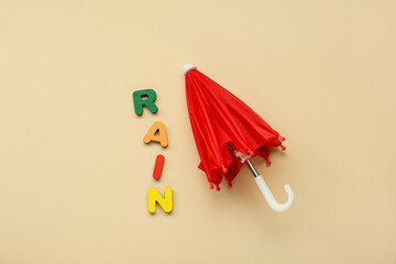 Red umbrella and word RAIN made of colorful letters on color background