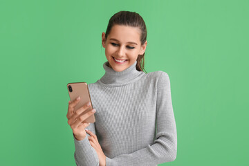 Beautiful happy young woman with mobile phone on green background