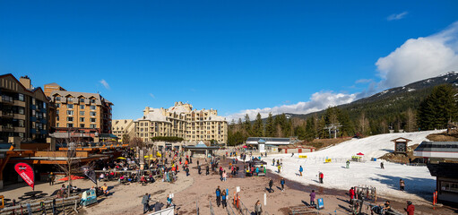 A panoramic image of the Whistler Village on a spring day with skiers on Whistler Mountain.