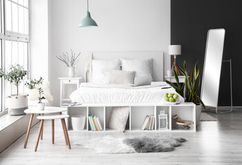 Stylish interior of light bedroom with comfortable bed and modern laptop