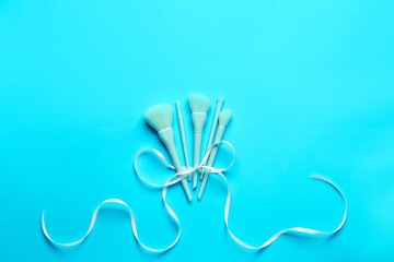 Composition with set of makeup brushes and ribbon on blue background