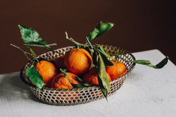 mandarin oranges in silver metal basket on white, brown background