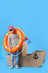 Cute little boy playing with cardboard ship on blue background