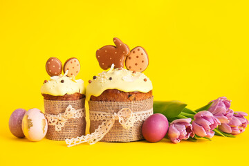Delicious Easter cakes decorated with cookies, flowers and painted eggs on yellow background
