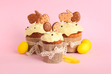 Delicious Easter cakes decorated with cookies and painted eggs on pink background