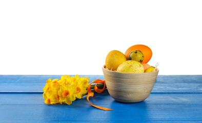 Bowl with painted Easter eggs and flowers on table against white background