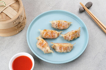 Korean Mandu Dumplings, made from flour dough and filled with seasoned chicken. Served on a plate with chili sauce
