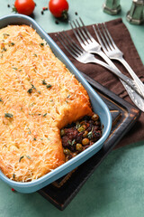 Baking dish with tasty Shepherd's pie on green background, closeup
