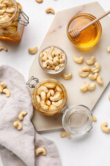 Jars of tasty cashew nuts with honey on light background