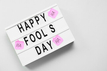 Board with text HAPPY FOOLS DAY and sticky notes on light background