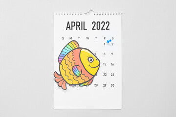 Calendar with marked date of April Fool's Day and paper fish on light background